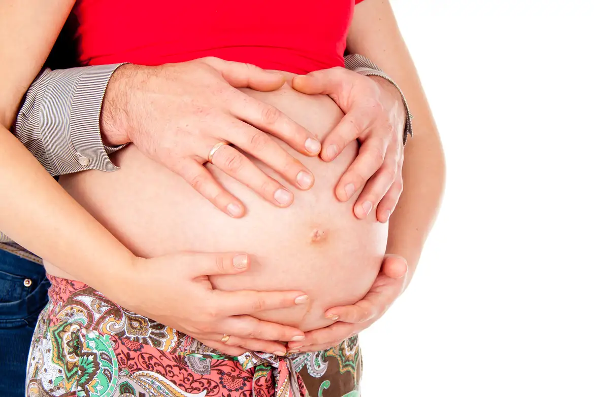 Gravid kvinde sammen med kæreste, som holder om hendes mave